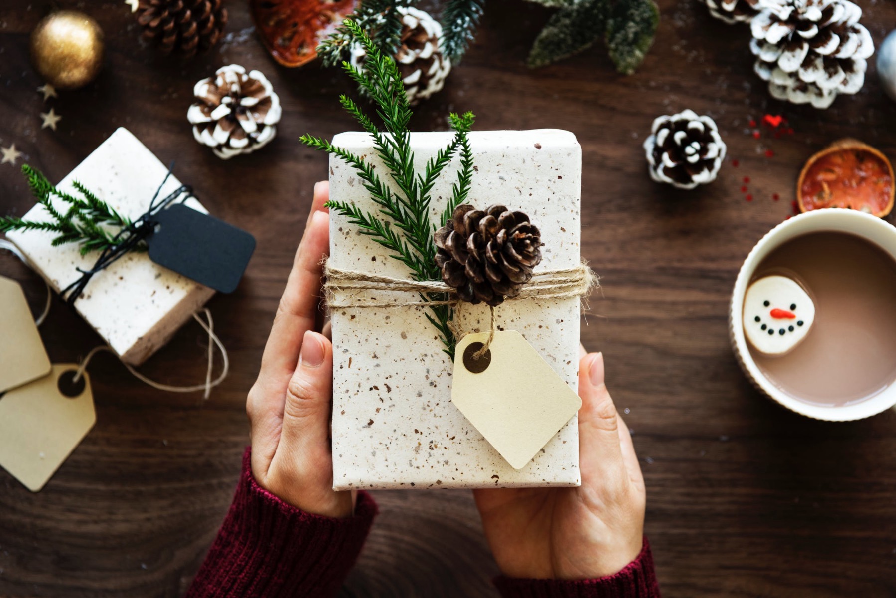 A present wrapped in which paper with a garnished with greenery and a pinecone 